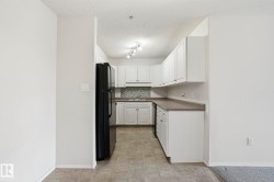 Kitchen featuring white cabinetry, dark countertops, black refrigerator, stainless steel dishwasher, and mosaic tile backsplash - 