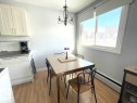 Bright kitchen dining area featuring light wood-finish flooring, white cabinetry, a built-in dishwasher, and a large window with white trim - 303 12223 82 Street, Edmonton, AB  - Indoor 