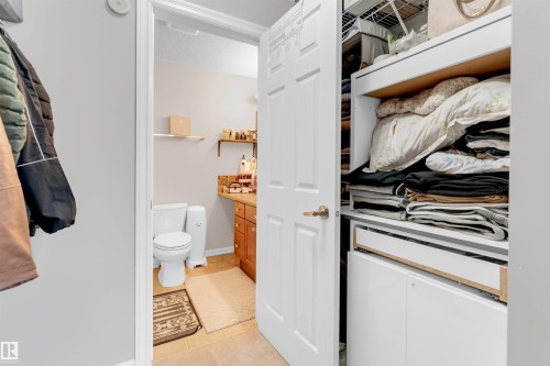 Compact water closet featuring a vanity with a light wood-finish cabinet, a white countertop, and a tiled backsplash - 201 4403 23 Street, Edmonton, AB - Indoor Photo Showing Bathroom