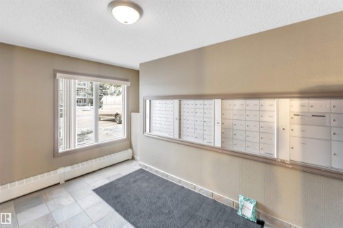 Entryway featuring a wall-mounted mailbox system, neutral wall paint, and a large window with roller shades - 201 4403 23 Street, Edmonton, AB - Indoor Photo Showing Other Room