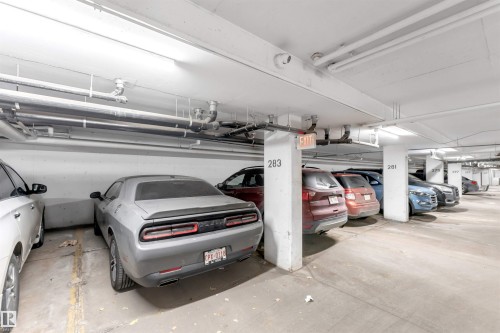 Subterranean parking garage featuring concrete flooring, numbered support columns, exposed overhead utility piping, and fluorescent lighting - 201 4403 23 Street, Edmonton, AB - Indoor Photo Showing Garage