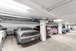 Subterranean parking garage featuring concrete flooring, numbered support columns, exposed overhead utility piping, and fluorescent lighting - 