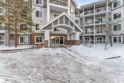 Multi-story building featuring an arched entrance canopy with stone-clad columns, multiple balconies with white railings, and a combination of light and dark siding - 201 4403 23 Street, Edmonton, AB - Outdoor With Balcony With Facade