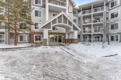 Multi-story building featuring an arched entrance canopy with stone-clad columns, multiple balconies with white railings, and a combination of light and dark siding - 