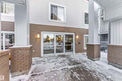 Building exterior featuring a glass entry, brick facade, white siding, and outdoor sconce lighting - 201 4403 23 Street, Edmonton, AB - Outdoor With Exterior
