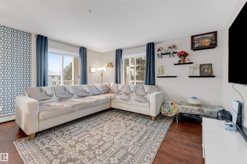 Spacious living area featuring wood-finish flooring, a geometric accent wall, and multiple windows providing ample natural light - 201 4403 23 Street, Edmonton, AB - Indoor Photo Showing Living Room