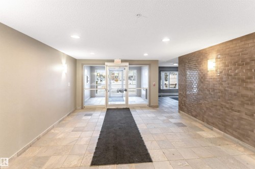 Foyer featuring light-toned tile flooring, recessed ceiling lighting, and a textured brick-patterned accent wall - 201 4403 23 Street, Edmonton, AB - Indoor Photo Showing Other Room