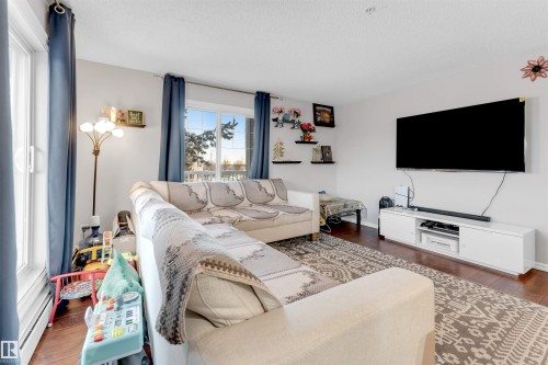 Living area featuring rich wood-finish flooring, white walls, and a large window with white trim - 201 4403 23 Street, Edmonton, AB - Indoor Photo Showing Living Room