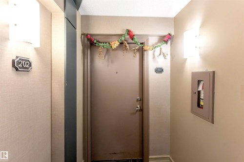 Entry door with wall-mounted sconces and a recessed fire extinguisher cabinet - 201 4403 23 Street, Edmonton, AB - Indoor Photo Showing Other Room