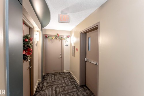 Hallway featuring patterned carpet flooring, neutral wall paint, and wall-mounted sconce lighting - 201 4403 23 Street, Edmonton, AB - Indoor Photo Showing Other Room