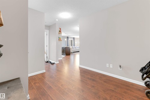 Hardwood-finish flooring extending throughout the main living areas, featuring light gray walls and white baseboards - 201 4403 23 Street, Edmonton, AB - Indoor