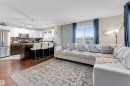 Open-concept living space featuring wood-finish flooring, a kitchen island with seating, stainless steel appliances, white upper cabinetry, and a patterned accent wall - 201 4403 23 Street, Edmonton, AB  - Indoor Photo Showing Living Room 