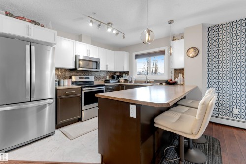 Contemporary kitchen featuring stainless steel appliances, white upper cabinetry, and dark lower cabinetry - 201 4403 23 Street, Edmonton, AB - Indoor Photo Showing Kitchen With Stainless Steel Kitchen