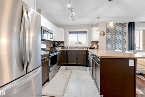Kitchen featuring stainless steel appliances, a multi-tone tile backsplash, and a breakfast bar peninsula with pendant lighting - 201 4403 23 Street, Edmonton, AB - Indoor Photo Showing Kitchen With Stainless Steel Kitchen