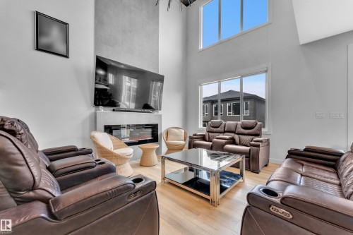 Spacious living area featuring a two-story ceiling, light wood-finish flooring, and expansive windows - 5722 Kootook Way, Edmonton, AB - Indoor Photo Showing Living Room With Fireplace