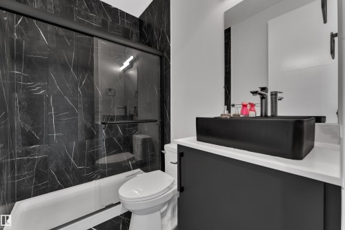 Bathroom featuring a black marble-patterned shower surround with a sliding glass door, a white bathtub, and a modern black vessel sink with a black faucet on a white countertop - 5722 Kootook Way, Edmonton, AB - Indoor Photo Showing Bathroom