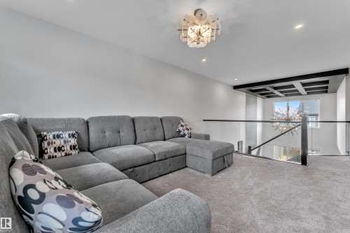 Upper-level landing featuring plush gray carpeting, a contemporary chandelier, recessed lighting, and a modern glass and metal railing system overlooking the lower level - 5722 Kootook Way, Edmonton, AB - Indoor