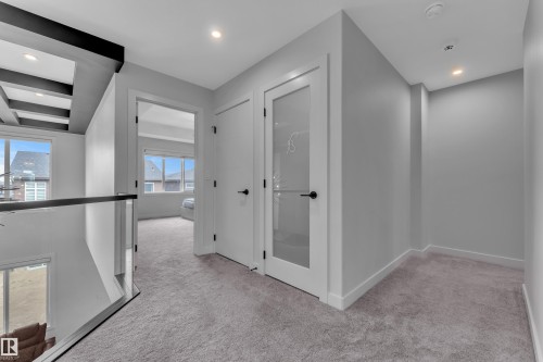Upper-level landing featuring plush gray carpeting, recessed lighting, a modern glass railing, and a white door with frosted glass paneling - 5722 Kootook Way, Edmonton, AB - Indoor Photo Showing Other Room