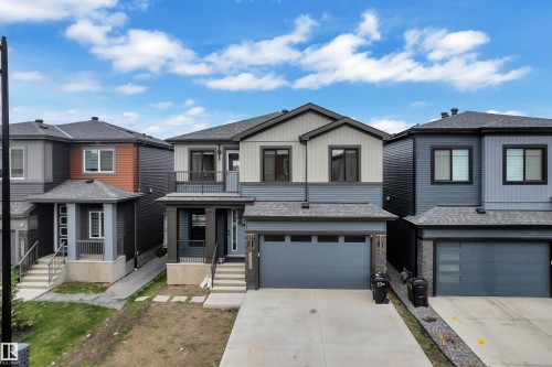 Contemporary home exterior featuring multi-toned siding, an integrated garage, an upper-level balcony with metal railing, a covered porch, and a concrete driveway - 5722 Kootook Way, Edmonton, AB - Outdoor With Balcony With Facade