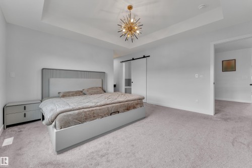 Recessed tray ceiling with a striking sputnik-style chandelier, light gray carpeting, and a modern barn door entry - 5722 Kootook Way, Edmonton, AB - Indoor Photo Showing Bedroom