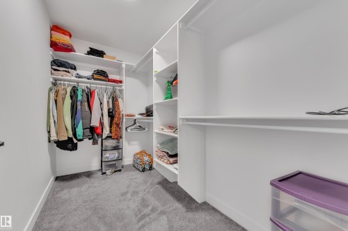 Spacious walk-in closet featuring white built-in shelving, multiple hanging rods, and light gray carpeting - 5722 Kootook Way, Edmonton, AB - Indoor With Storage