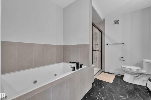 Soaking tub with black hardware, surrounded by large format light grey wall tiles - 5722 Kootook Way, Edmonton, AB - Indoor Photo Showing Bathroom