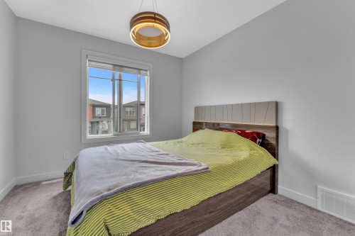 Bright room featuring a large window, plush carpet flooring, light gray wall paint, white baseboards, and a contemporary ceiling light fixture - 5722 Kootook Way, Edmonton, AB - Indoor Photo Showing Bedroom