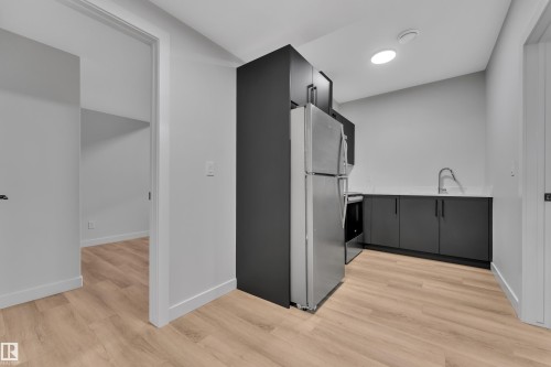 Modern kitchen area featuring stainless steel appliances, dark cabinetry, and light wood-finish flooring - 5722 Kootook Way, Edmonton, AB - Indoor