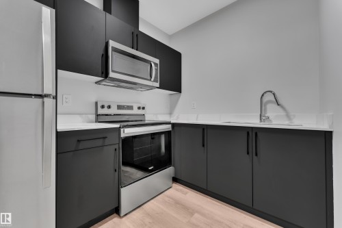 Modern kitchen featuring dark cabinetry, light countertops, stainless steel appliances including a refrigerator, range, and microwave, and wood-finish flooring - 5722 Kootook Way, Edmonton, AB - Indoor Photo Showing Kitchen