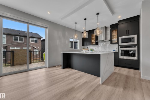 Modern kitchen featuring dark cabinetry with glass accents, a large waterfall island with a light-toned countertop, and stainless steel appliances - 5722 Kootook Way, Edmonton, AB - Indoor Photo Showing Kitchen With Upgraded Kitchen