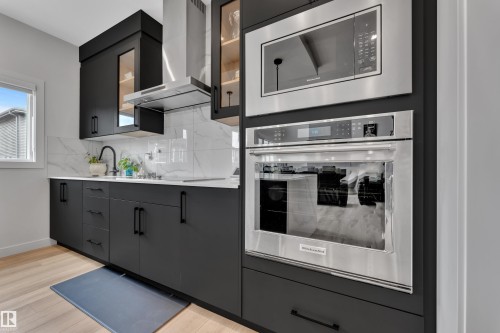 Modern kitchen featuring matte black cabinetry with black hardware, white countertops, and a full-height marble-patterned backsplash - 5722 Kootook Way, Edmonton, AB - Indoor Photo Showing Kitchen