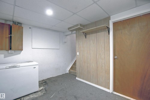 Utility space featuring white painted block walls, wood-paneled wall accents, a drop ceiling, and a wooden door - 11 14120 80 Street, Edmonton, AB - Indoor