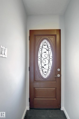 Entry door featuring an oval decorative glass insert with wrought iron detailing, a dark wood-finish panel, and brushed nickel hardware - 11 14120 80 Street, Edmonton, AB - Indoor Photo Showing Other Room