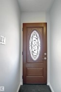 Entry door featuring an oval decorative glass insert with wrought iron detailing, a dark wood-finish panel, and brushed nickel hardware - 
