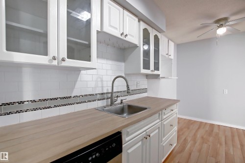 Kitchen featuring wood-finish countertops, stainless steel sink with a high-arc faucet, and white subway tile backsplash with a decorative mosaic accent - 11 14120 80 Street, Edmonton, AB - Indoor Photo Showing Kitchen