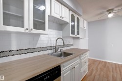 Kitchen featuring wood-finish countertops, stainless steel sink with a high-arc faucet, and white subway tile backsplash with a decorative mosaic accent - 
