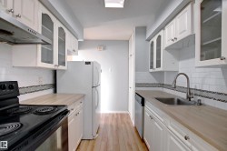 Galley kitchen featuring light wood-finish countertops, white cabinetry with some glass-front doors, white subway tile backsplash with a mosaic accent, stainless steel sink, and wood-finish flooring - 