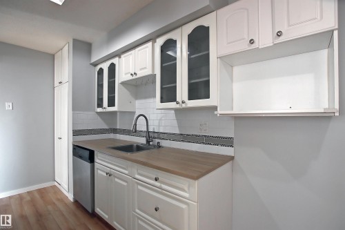 Kitchen featuring white cabinetry, wood-finish countertops, stainless steel sink with a gooseneck faucet, subway tile backsplash with decorative mosaic accent, and wood-finish flooring - 11 14120 80 Street, Edmonton, AB - Indoor Photo Showing Kitchen