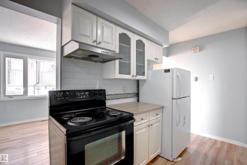 Kitchen featuring white cabinetry, a black range with an overhead vent, a white refrigerator, and light wood-finish flooring - 11 14120 80 Street, Edmonton, AB - Indoor Photo Showing Kitchen