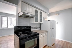 Kitchen featuring white cabinetry, a black range with an overhead vent, a white refrigerator, and light wood-finish flooring - 