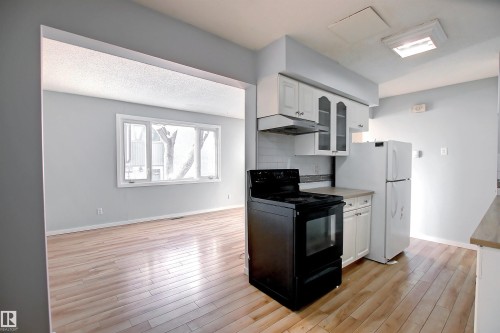 Light wood-finish flooring throughout, white upper and lower cabinetry, white subway tile backsplash, and a large window with white trim - 11 14120 80 Street, Edmonton, AB - Indoor Photo Showing Kitchen