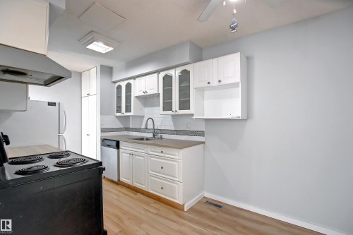 Kitchen featuring white cabinetry, a built-in dishwasher, wood-finish flooring, a tile backsplash, and a ceiling fan - 11 14120 80 Street, Edmonton, AB - Indoor Photo Showing Kitchen