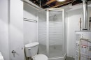 Compact bathroom featuring a corner shower with frosted glass panels, a white toilet, and exposed ceiling joists - 11 14120 80 Street, Edmonton, AB  - Indoor Photo Showing Bathroom 