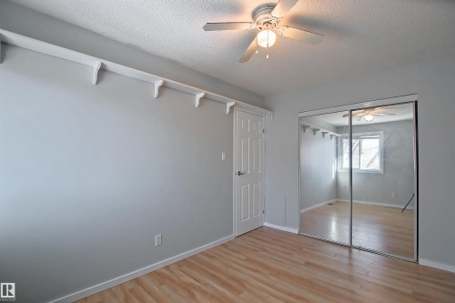 Room featuring wood-finish flooring, a ceiling fan with integrated lighting, a paneled door, and mirrored sliding closet doors - 11 14120 80 Street, Edmonton, AB - Indoor Photo Showing Other Room