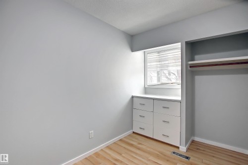 Built-in cabinetry with six drawers, wood-finish flooring, recessed window, window blinds, and built-in closet shelving with hanging rod - 11 14120 80 Street, Edmonton, AB - Indoor Photo Showing Other Room