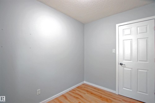 Interior space featuring light gray walls, wood-finish flooring, white baseboards, and a white six-panel door with a silver-tone handle - 11 14120 80 Street, Edmonton, AB - Indoor Photo Showing Other Room