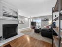 Living area featuring a fireplace with a tile surround and hearth, wood-finish flooring, and a large window - 165 2703 79 Street, Edmonton, AB  - Indoor Photo Showing Living Room With Fireplace 
