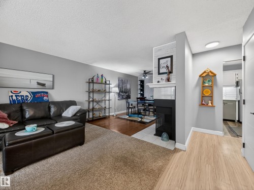Living area featuring a fireplace with a white mantel and shiplap-style accent, light-toned wood-finish flooring, and a carpeted section - 165 2703 79 Street, Edmonton, AB - Indoor