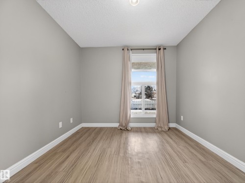 Bright room featuring wood-finish flooring, light gray walls, white baseboards, and a window with curtains - 165 2703 79 Street, Edmonton, AB - Indoor Photo Showing Other Room