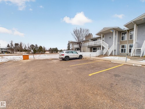 Paved parking lot with yellow stripe delineation providing direct access to multi-level residential units featuring light-toned siding and white exterior railings - 165 2703 79 Street, Edmonton, AB - Outdoor